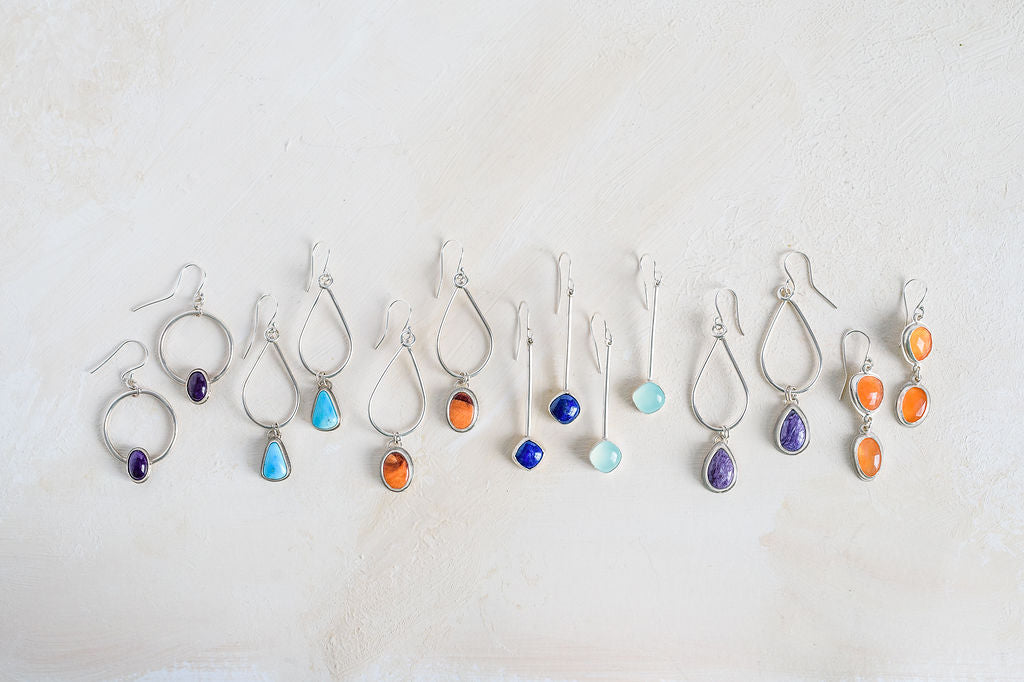 Collection of handmade gemstone earrings in various colours, sugilite, turquoise, orange spiny oyster shell, lapis lazuli, seafoam chalcedony, purple chariote  and orange carnelian Handmade by Laura De Zordo Jewellery in the UK